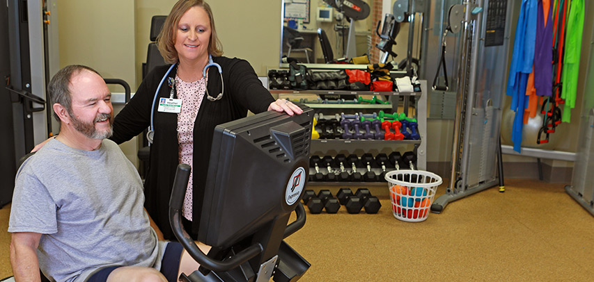 A physical therapist adjusts the settings on screen for a patient seated on an exercise bike in the Wellness Center.