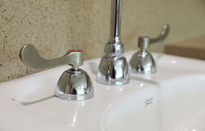 Close-up of copper-coated faucet handles next to a sparkling clean sink.