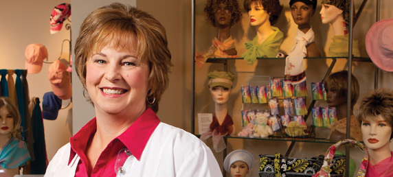 LMC nurse navigator Kelly Jeffcoat smiling inside of Becky’s Place Boutique, a hospital-run boutique for women recovering from cancer and needing wigs, hats, scarves and more, which can be seen in the background.